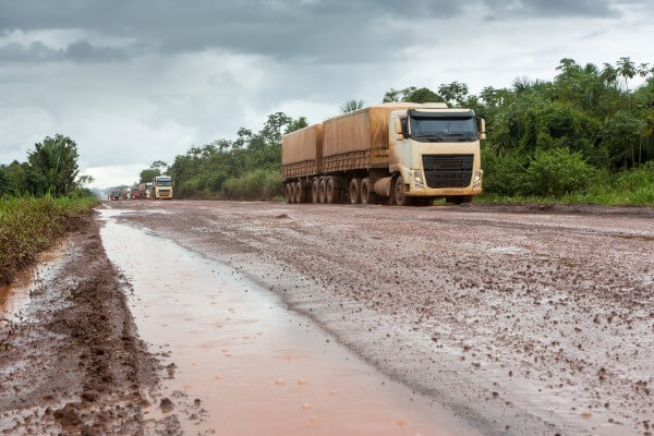 Caminhões realizando transporte da soja no Brasil em rodovias em péssimas condições.