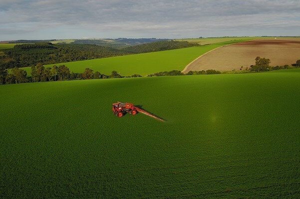 Visão aérea de maquinário aplicando herbicidas no campo de soja.