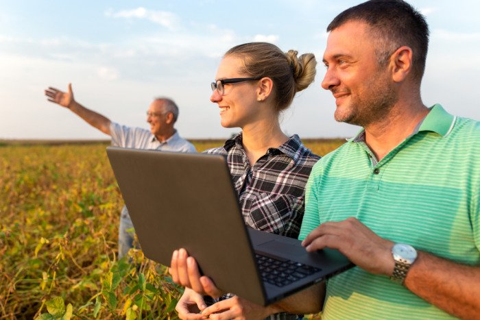 sucessão rural: dois homens e uma mulher, olhando para o campo enquanto um dos homens segura um notebook